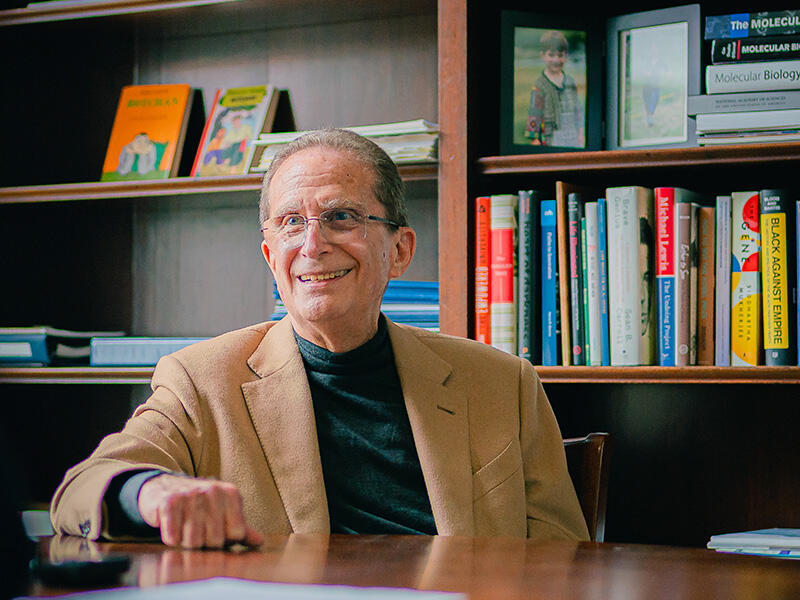 Michael Botchan leans on a table in front of a wooden bookshelf