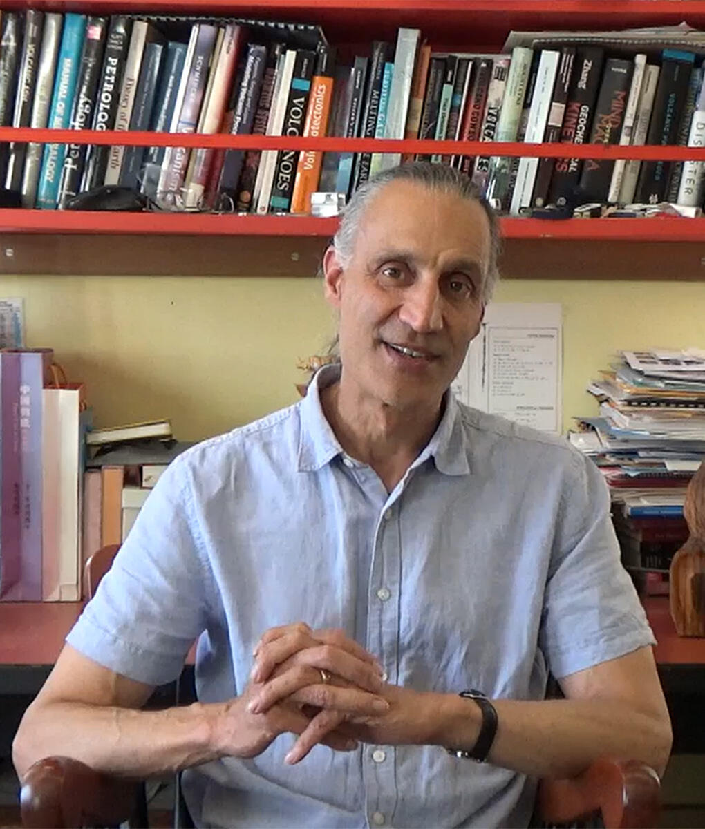 Michael Manga sits at a chair in his office with a telescope and books in the background.