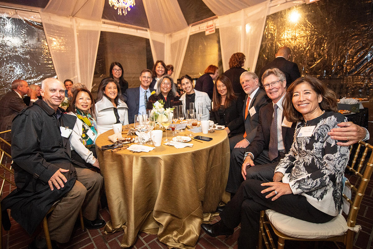 A group of people sit with the Morgans around a table in a tent
