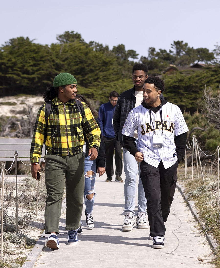 A group of students walk toward the camera on a sandy path