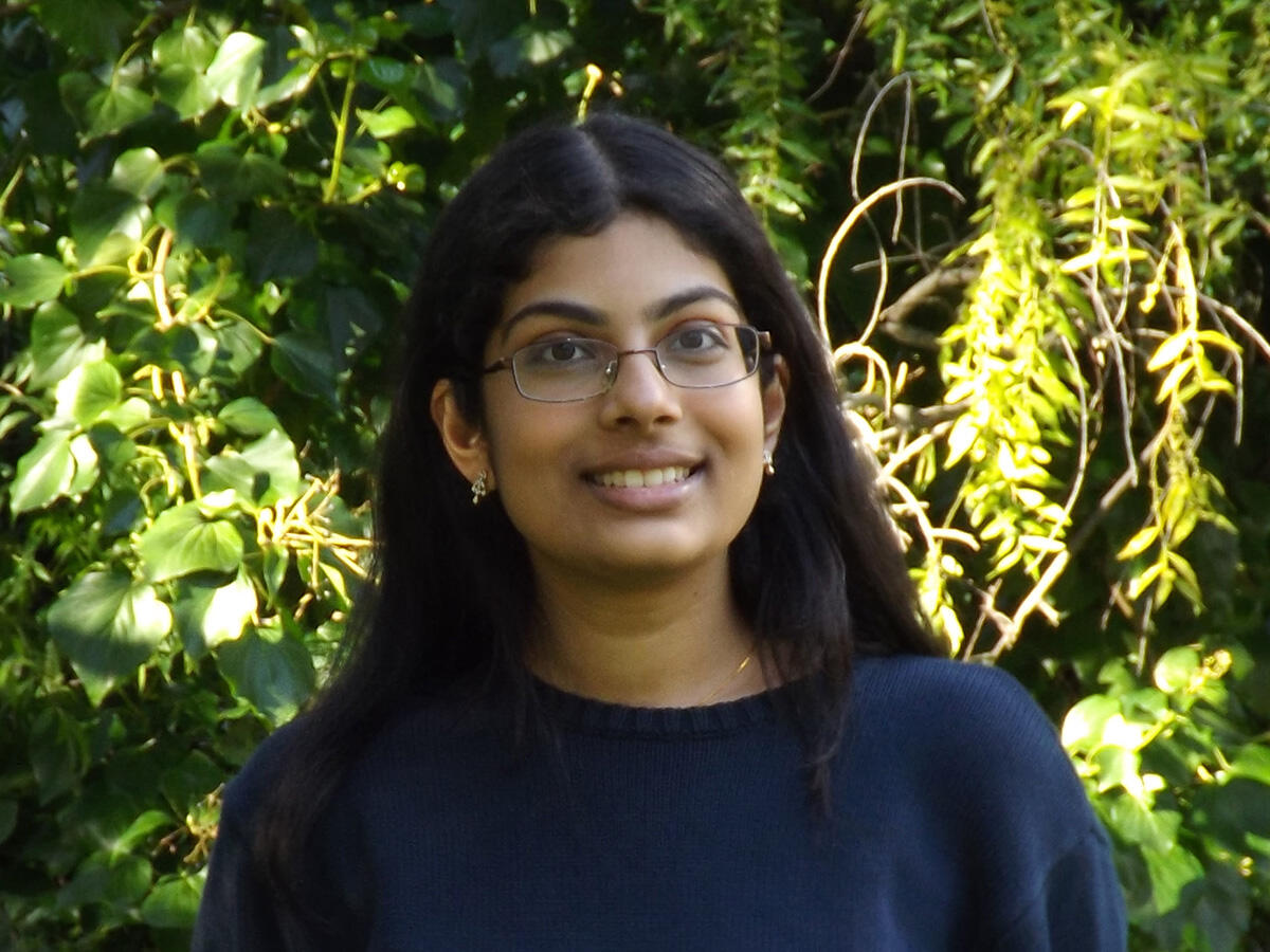 A headshot of Neeraja Sripada in a sweater in front of some ivy and trees