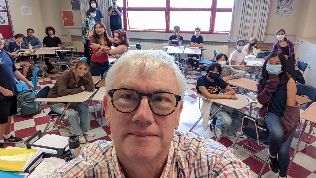 Photo of a man with glasses and white hair teaching in a classroom of teenagers