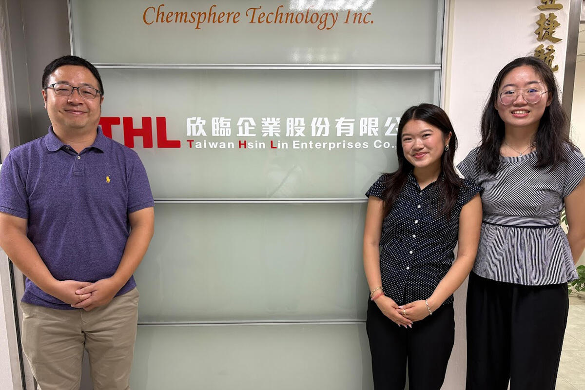 A man and two female students pose next to a sign that reads "THL Taiwan Hsin Lin Enterprises Co."