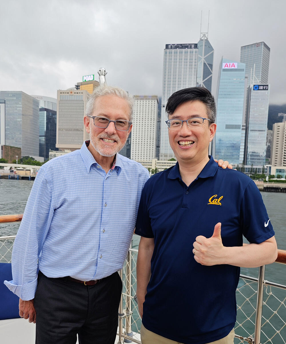 Two men smile for the camera in front of a city waterfront