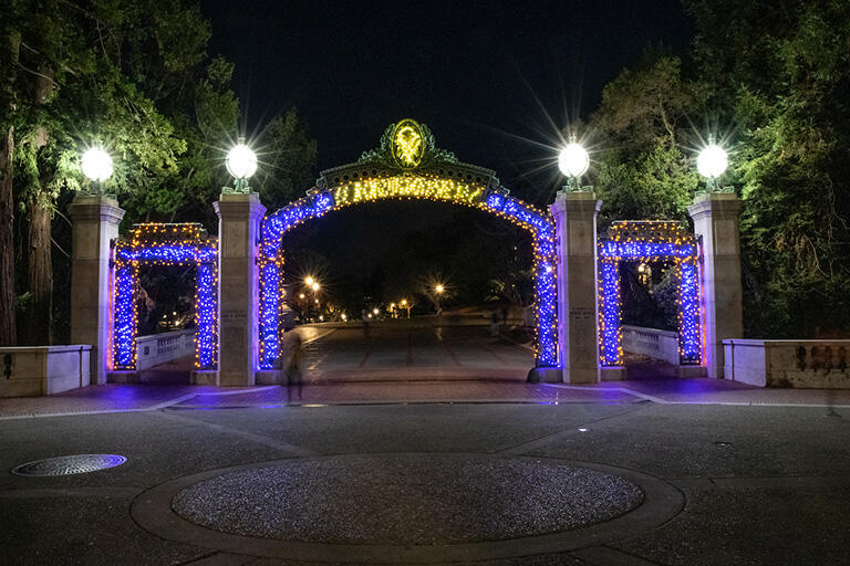 Sather Gate at night, glowing with blue and yellow lights