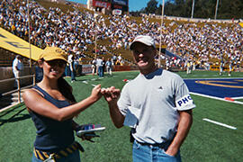 A woman and man lock pinky fingers on the sidelines of a Cal football game