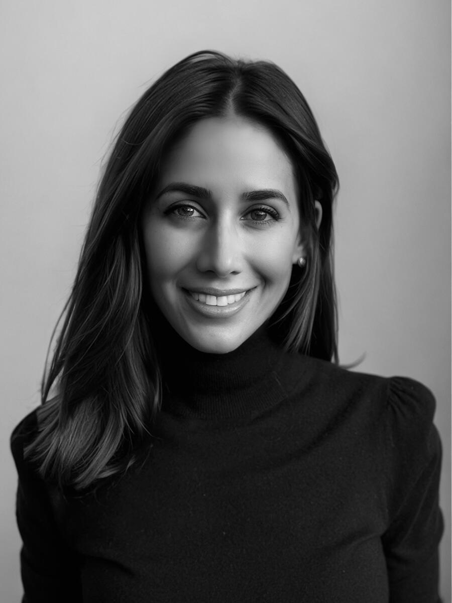 A black-and-white headshot of a smiling woman with dark hair and a dark sweater