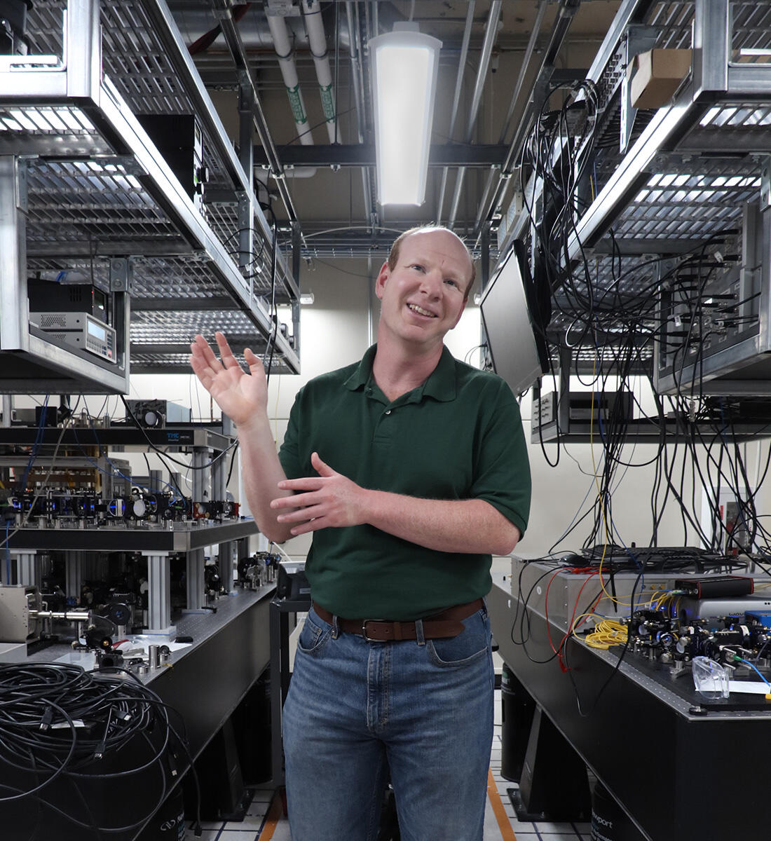 A man in a green polo shirt and jeans gestures to nearby equipment
