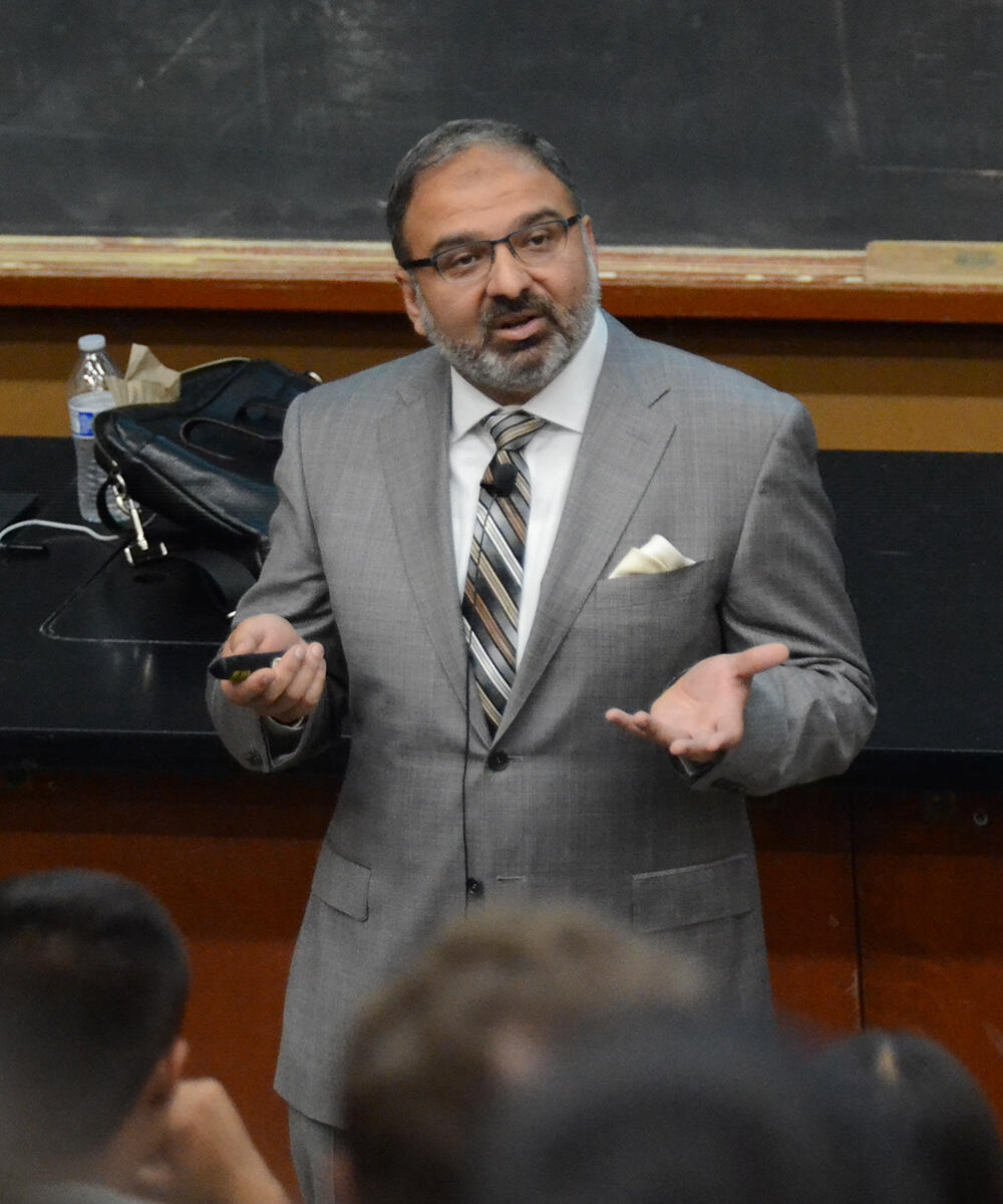 Irfan Siddiqi, wearing a suit, talks to a classroom of students, faculty, and staff