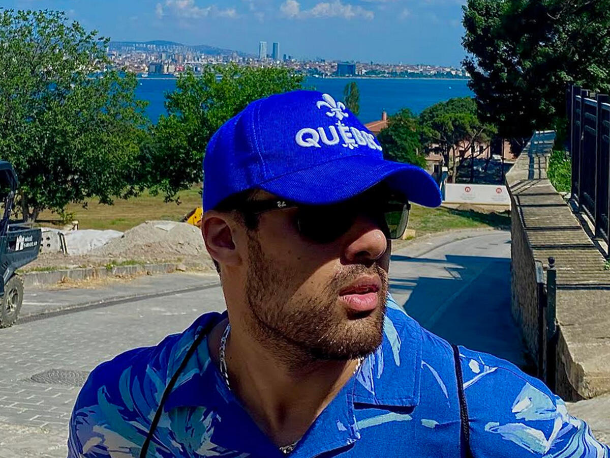 A photo of Sohaib Butt outdoors on a sunny day with sunglasses and a blue hat that reads "Quebec"