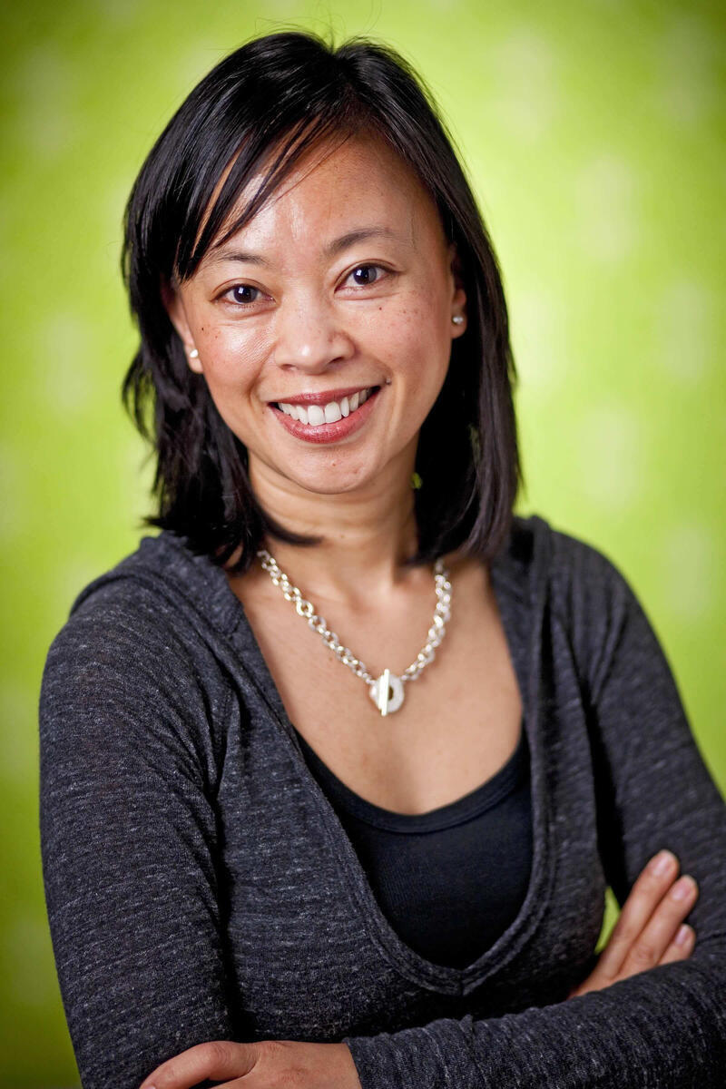 Headshot of Aileen Zerrudo wearing dark shirt, silver necklace against a green background