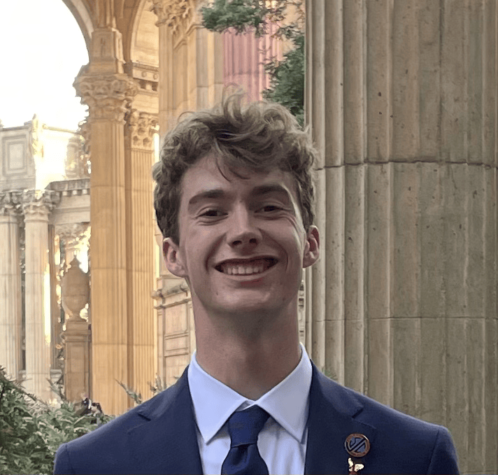 Man with curly blonde hair in a suit smiling