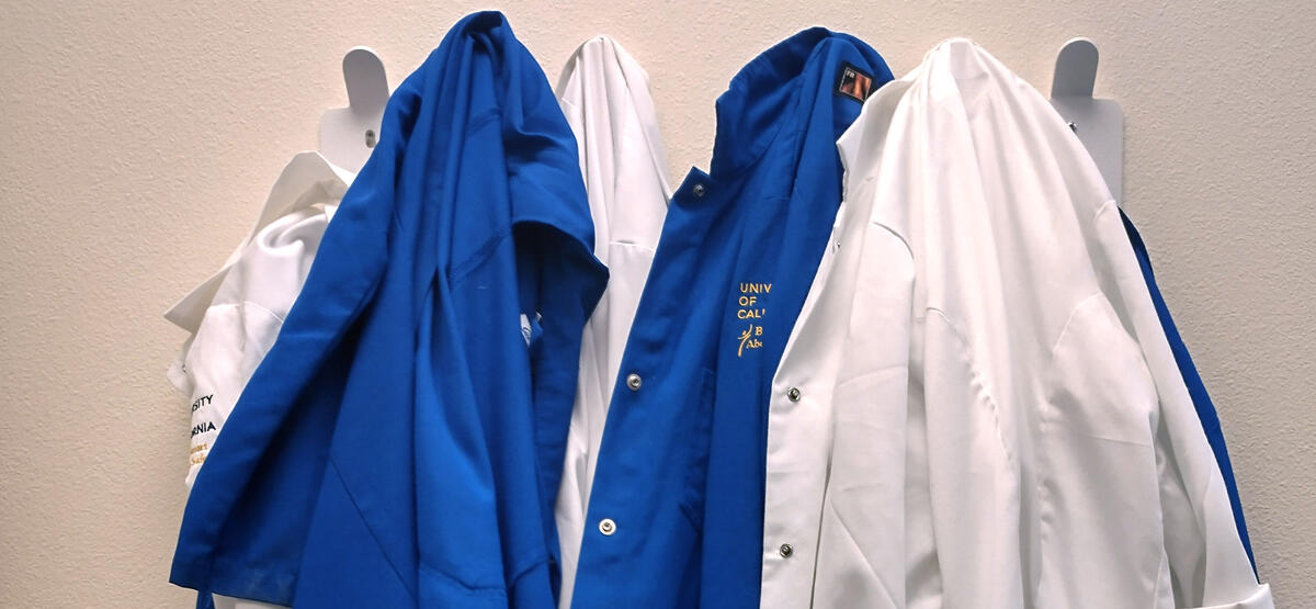 Blue and white lab coats hang on a coat rack.