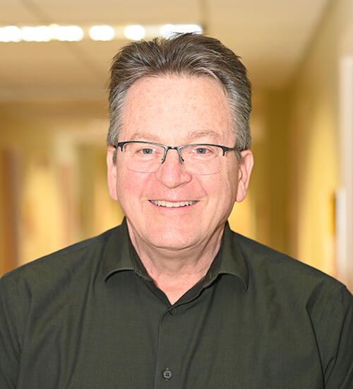 Headshot of Mark Sandberg; person wearing a dark collared shirt and wearing glasses