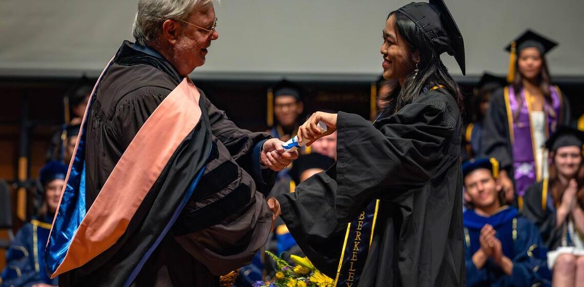 Graduate is awarded diploma with a handshake at commencement
