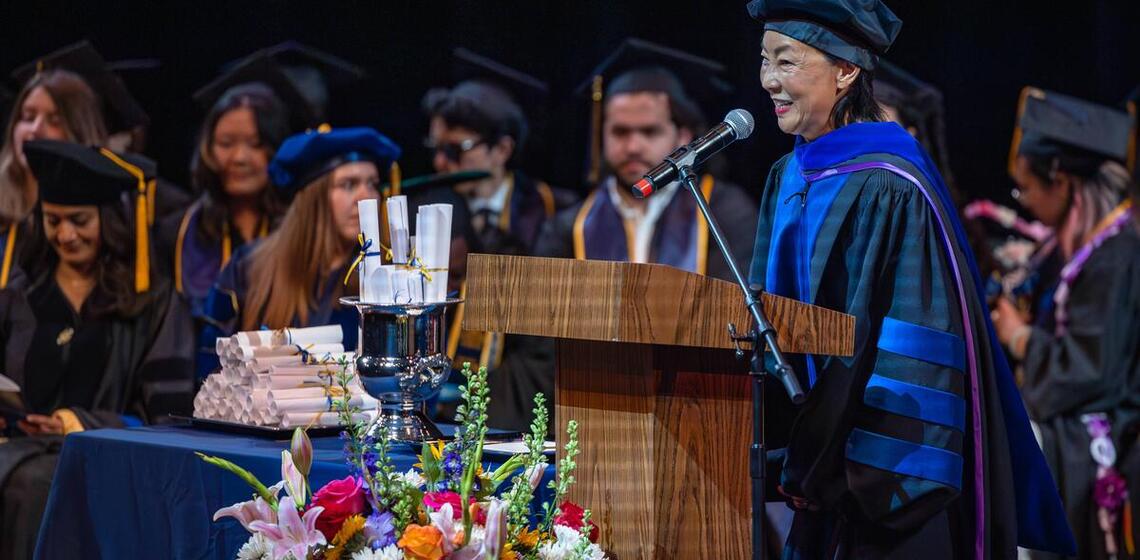 Woman in regalia speaking at commencement podium