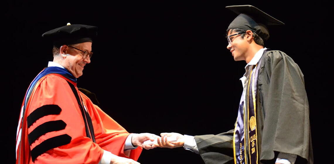 Graduate is handed diploma on stage by faculty