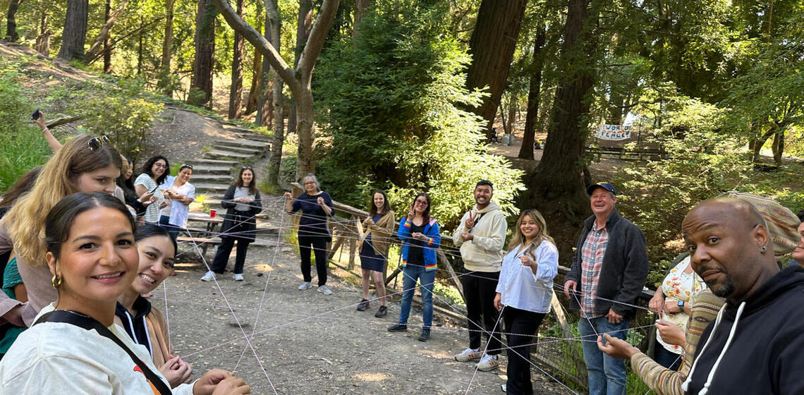 Group outdoors holding a string as part of a team building exercise.