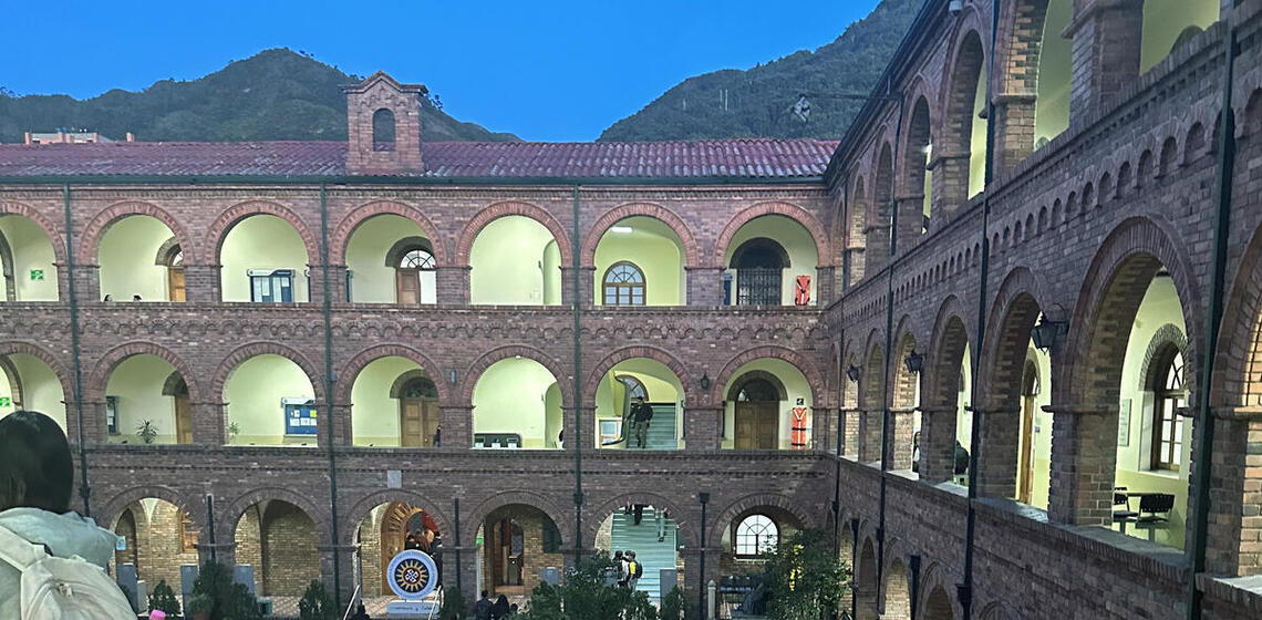 A university building with brick arches and a curved tile roof, lit up in the early evening