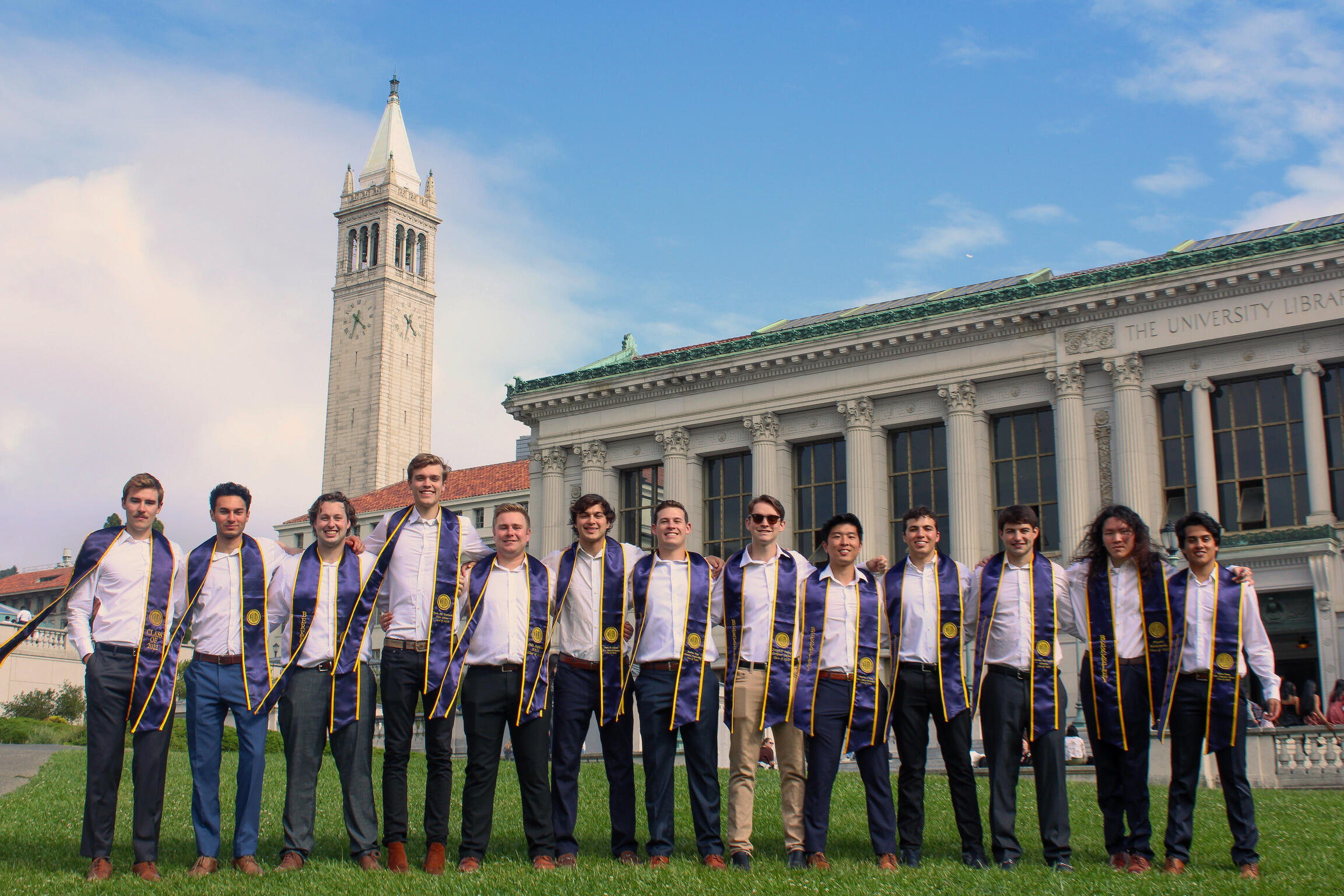 Group of graduates stand in front of the University Library and Campanile