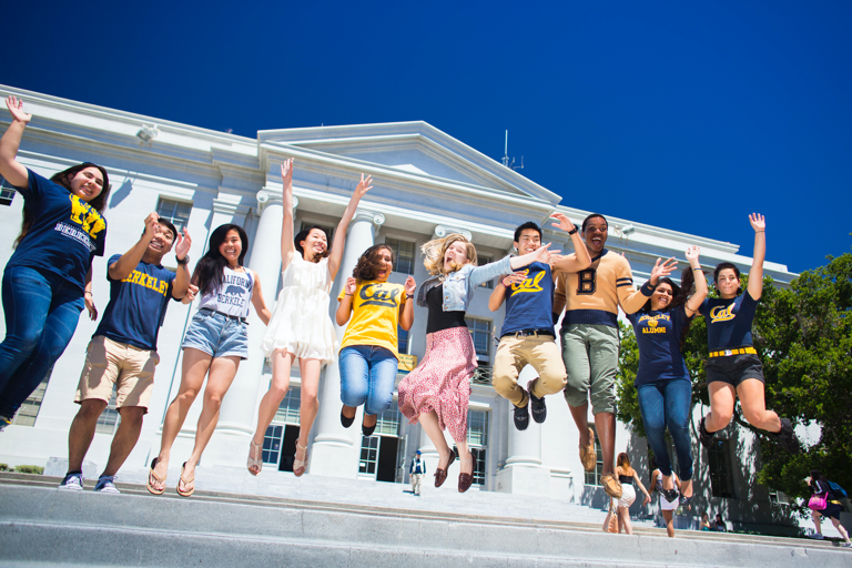 Large group of students jumping on the steps in front of a grand building