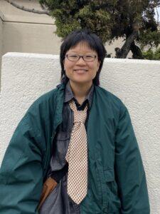 Person wearing glasses, green jacket and a beige tie