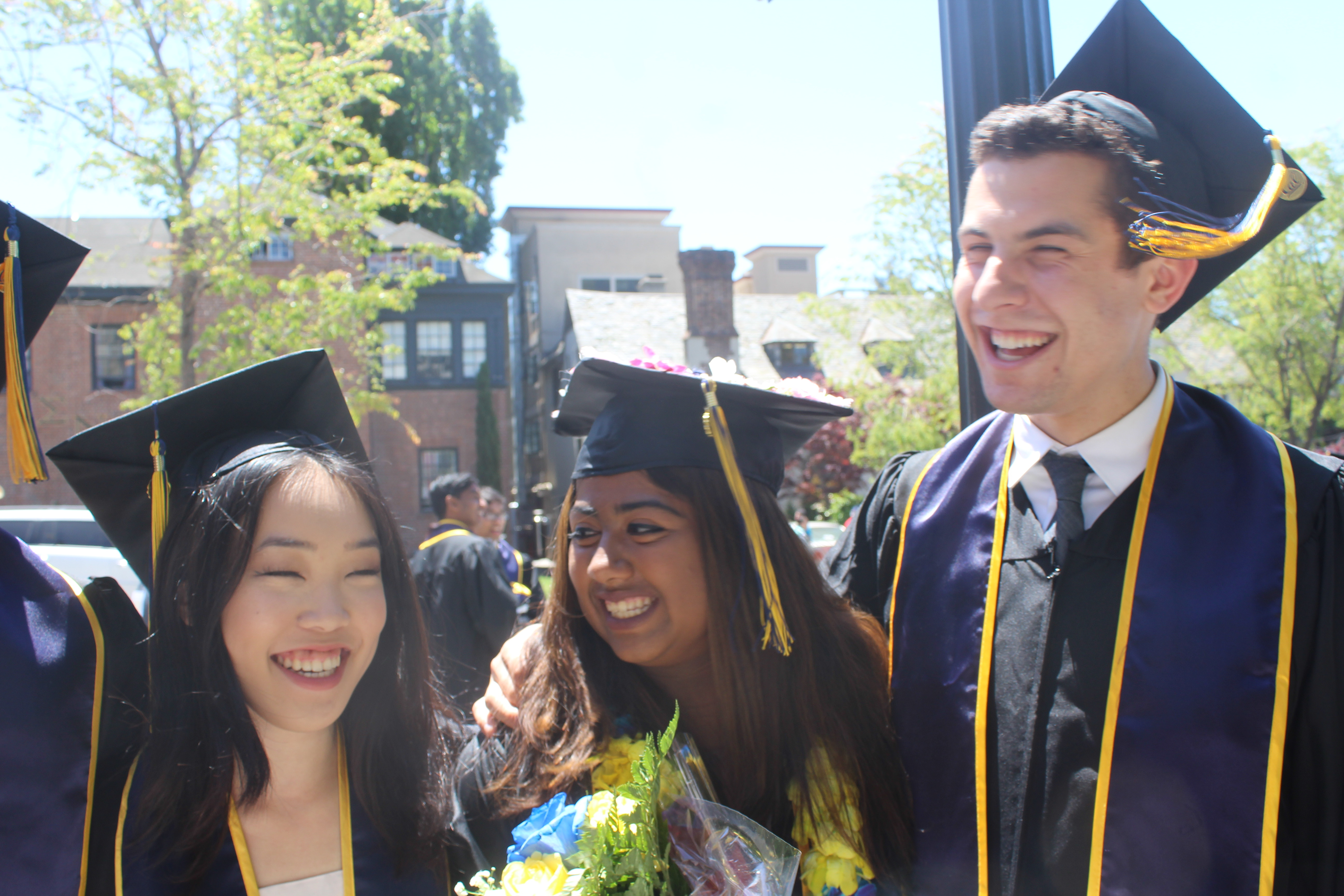 Three friends dressed in commencement gowns smile and laugh together