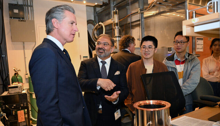 two men talking in a lab surrounded by young people