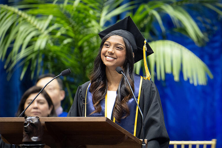 Graduate wearing cap and gown speaks from a lectern