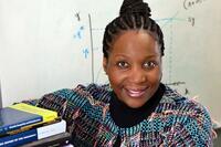 Economist Lisa Cook smiling at camera in front of a whiteboard, and leaning next to books