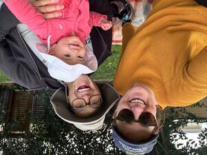 Two adults pose with a baby, all smiling and wearing hats outdoors