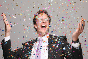 Frank Cahill smiles and holds up his hands as colorful confetti is all around him, showing the fun, playful spirit of the spelling bee and the people who run it