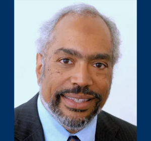 Headshot of man with grey hair and beard; wearing a suit and tie