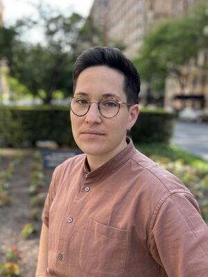Headshot of person wearing a brown buttoned shirt next to a blue graphic background