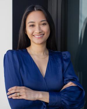 Woman with long dark hair, wearing a blue blouse, with her arms crossed