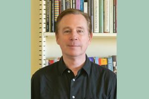 Headshot of Professor Whitney Davis wearing a black button down shirt, standing in front of a bookshelf