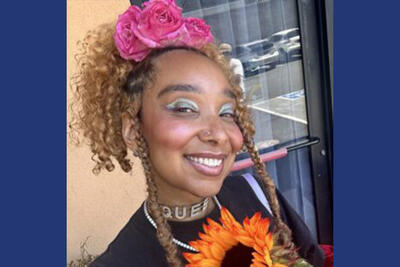 Woman with pink roses in her curly brown hair smiles at camera