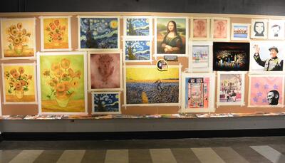 A wall in an art exhibition of replicas of many famous artworks, like van Gogh's Sunflowers and da Vinci's Mona Lisa