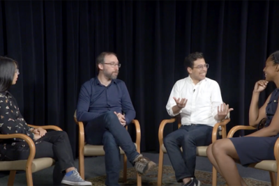 Four people sitting in chairs, talking in front of a black background