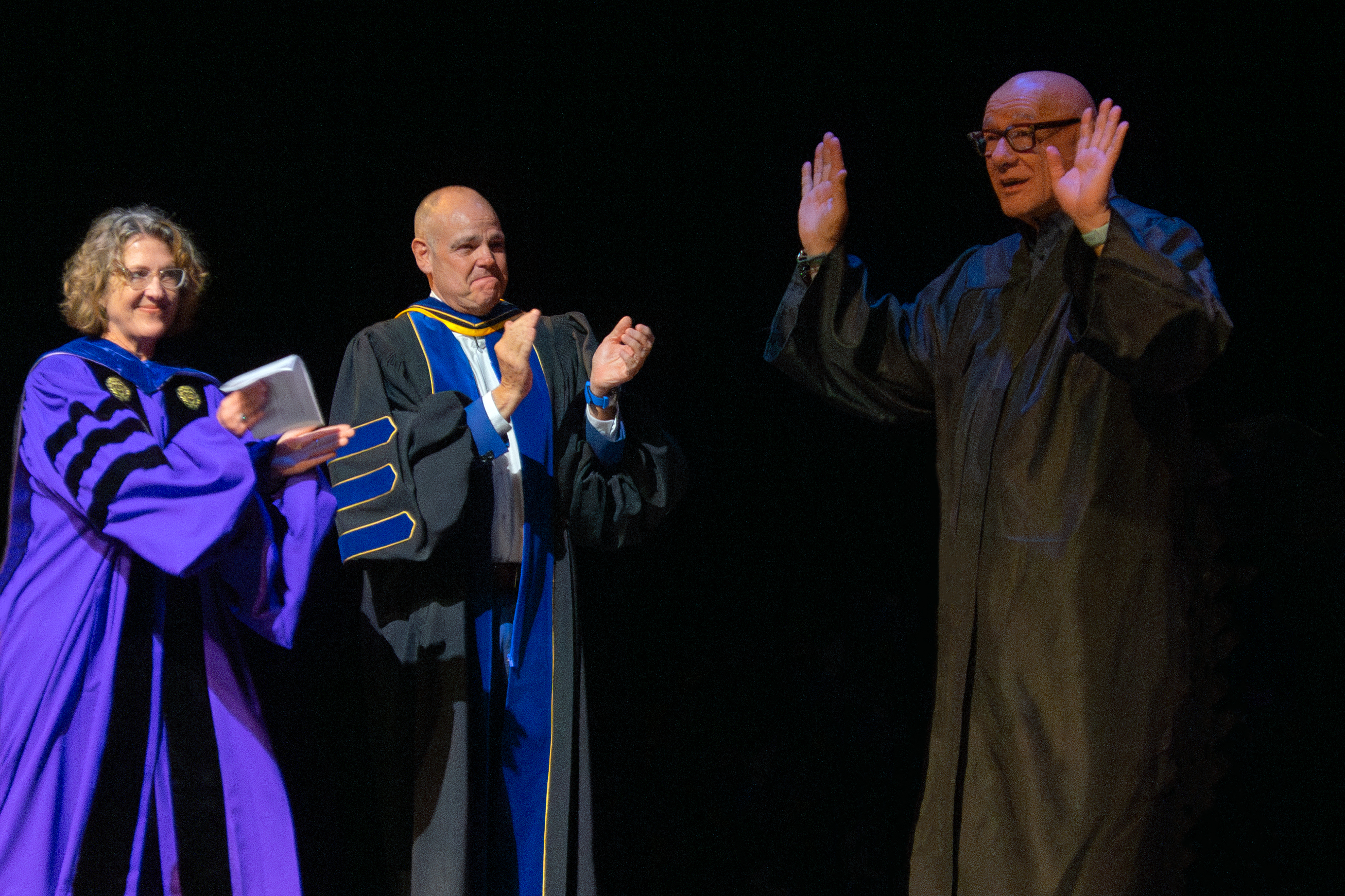Faculty applaud a colleague during commencement, who holds his arms up