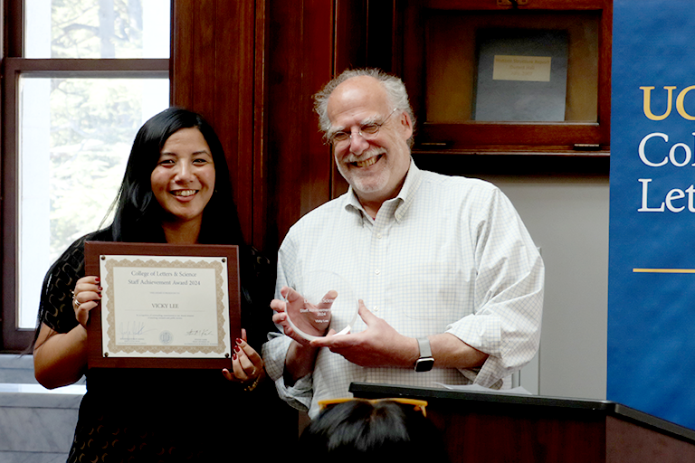 A woman and a man stand together, holding awards